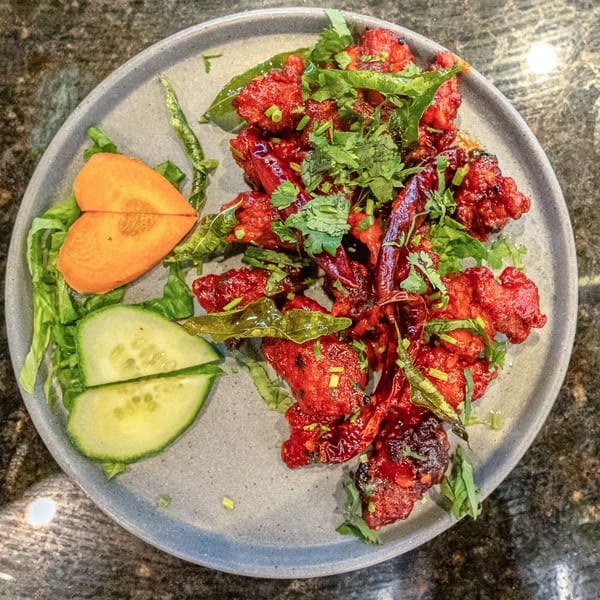 Rangoli Restaurant's Chicken 65, a vibrant red Indian dish with herbs, chili, and a side salad.