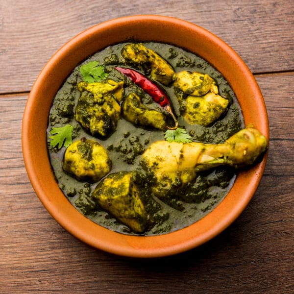 Rangoli Restaurant's Palak Chicken, a vibrant green Indian curry with chicken pieces and a red chili.