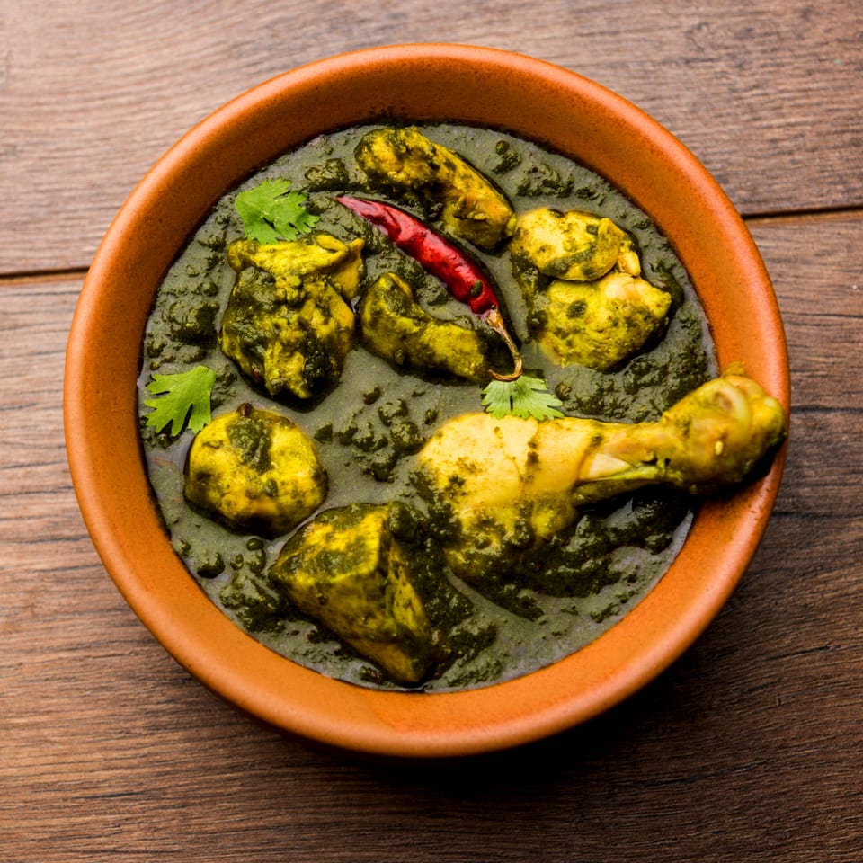 Rangoli Restaurant's Palak Chicken, a vibrant green Indian curry with chicken pieces and a red chili.