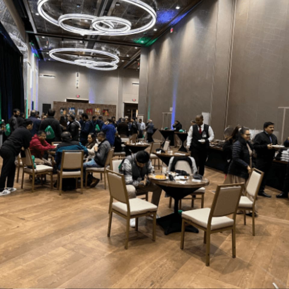 Guests gather in a large, modern event space with circular chandeliers and a buffet line.
