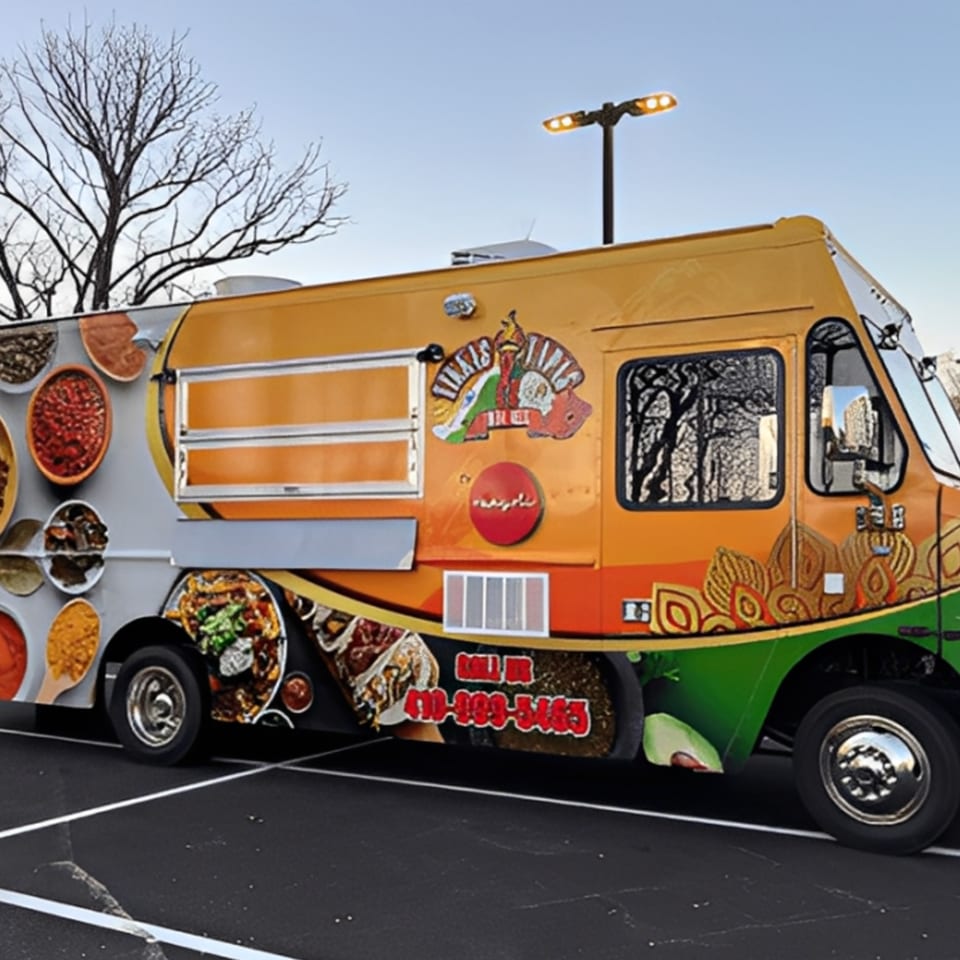 Rangoli Restaurant's vibrant orange and green Indian food truck with food graphics in a parking lot.