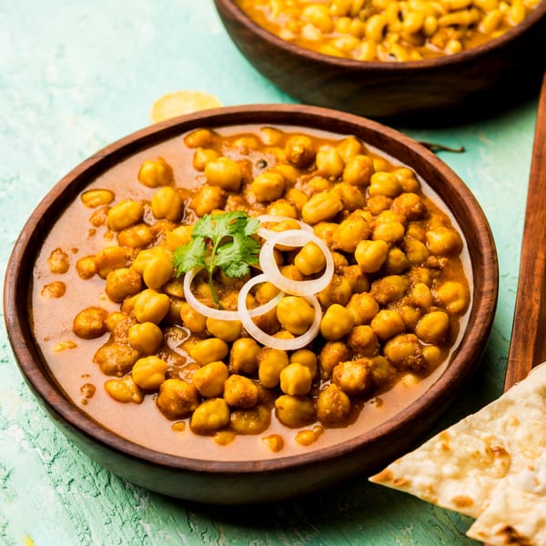 A wooden bowl of chana masala, garnished with cilantro and onion, with naan bread.