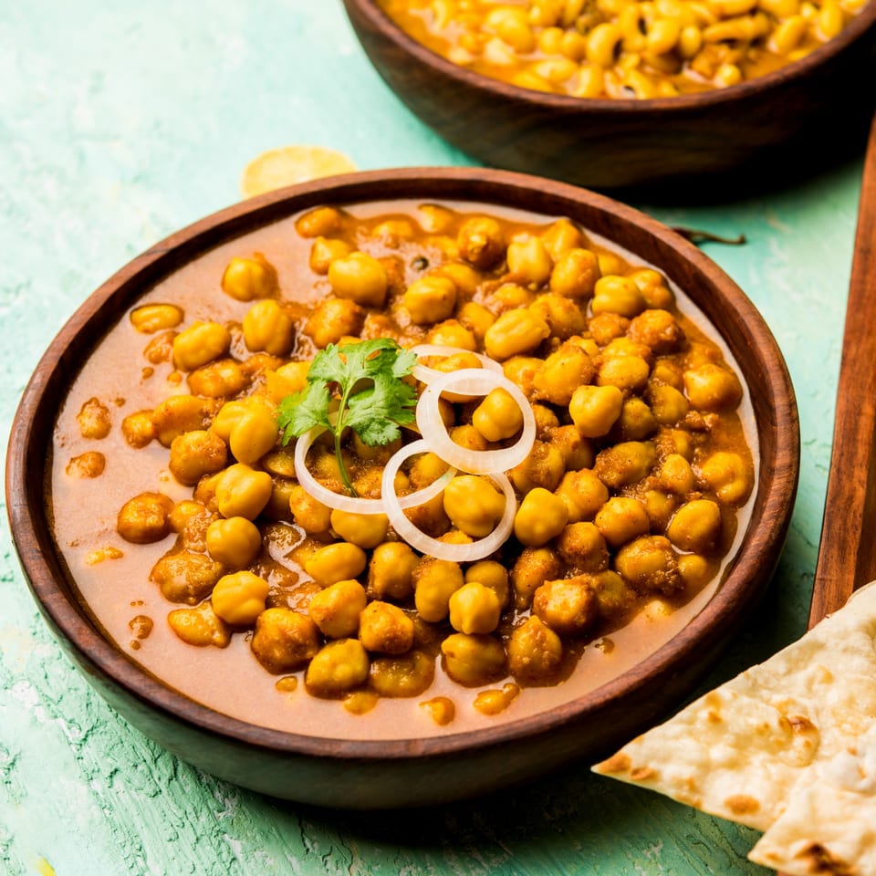 A wooden bowl of chana masala, garnished with cilantro and onion, with naan bread.