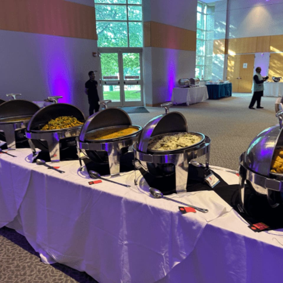 A buffet line of Indian food in chafing dishes with purple uplighting in a large event space.