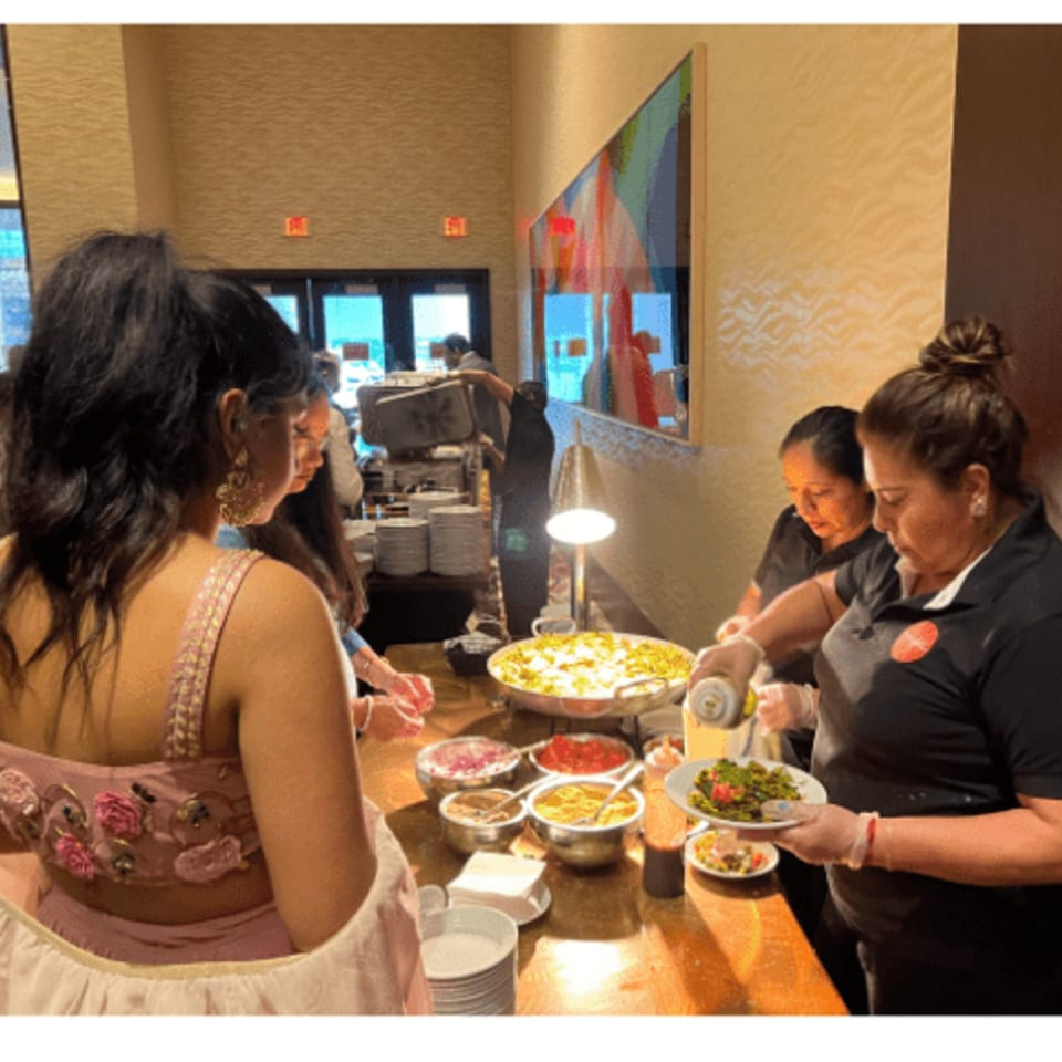 A server at Rangoli Restaurant plates Indian food for a guest at a buffet line.