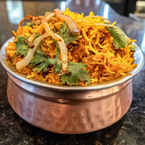 Rangoli Restaurant's Indian biryani, a vibrant yellow rice dish with fried onions and fresh cilantro.
